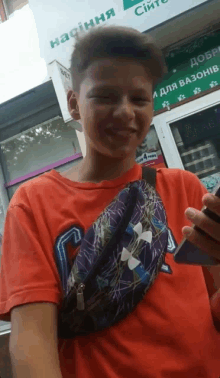 a boy wearing an under armour fanny pack smiles while holding a cell phone