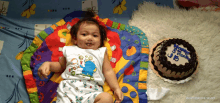 a baby is laying on a colorful blanket next to a cake that says ' happy 3rd birthday ' on it