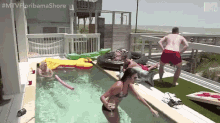 a woman in a bikini is jumping into a swimming pool while a man in red shorts watches .