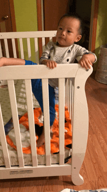 a baby standing in a white crib with a blanket on the floor