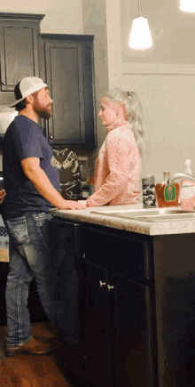 a man and a woman stand in front of a kitchen sink with a bottle of dawn dish soap on the counter