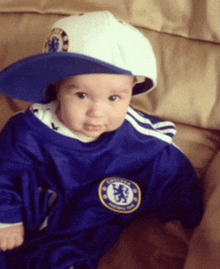 a baby wearing a blue chelsea jersey and a white hat