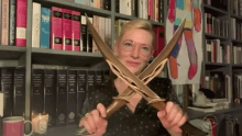 a woman is holding a pair of swords in front of a bookshelf that has a book titled " the bible " on it