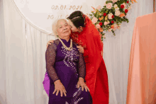 a woman in a red dress kisses an older woman in a purple dress on the cheek