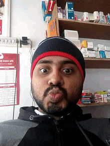 a man with a beard wearing a black and red beanie stands in front of a shelf with extreme pleasure