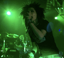 a woman singing into a microphone wearing a black shirt that says dreads