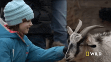 a girl petting a goat with a national geographic logo in the corner
