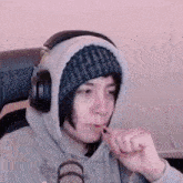 a person wearing headphones and a beanie is brushing their teeth in front of a microphone .