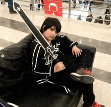 a young boy is sitting on a couch holding a large black sword