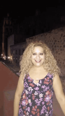 a woman wearing a floral top is smiling in front of a stone wall