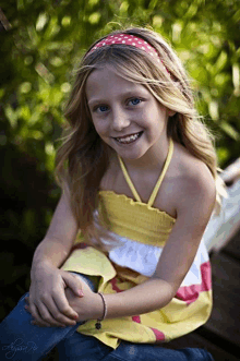 a young girl wearing a red headband and a yellow top smiles for the camera