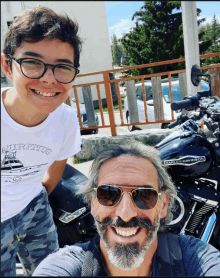 a man wearing sunglasses and a harley davidson shirt stands next to a boy