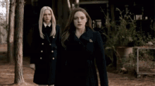 two women in black coats are standing next to each other in the woods .