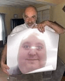 a man with a beard is holding a picture of his face .