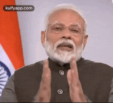 a man with a beard and glasses is giving a speech while standing in front of an indian flag .