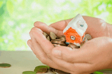 a person is holding a small house and a pile of coins in their hands