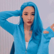 a woman with blue hair is wearing a blue sweater and giving a peace sign