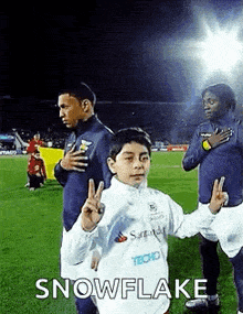 a young boy is giving a peace sign on a soccer field while standing next to a group of soccer players .