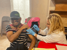 a man is getting an injection from a woman who is wearing gloves and a green hat that says campbell 's