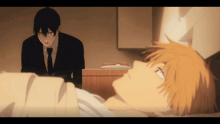 a man in a suit and tie is standing next to a man laying in a bed