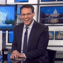 a man in a suit and tie is sitting at a desk with a mug that says msnbc on it