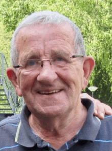 an older man wearing glasses and a striped shirt smiles for the camera