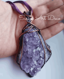 a hand holding a purple necklace with the words sirius art deco written on it