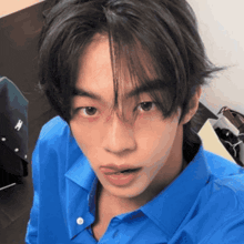 a young man wearing a blue shirt is looking at the camera