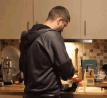 a man in a black jacket is cooking in a kitchen with a book on the counter that says " cooking "