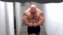 a bald man with a tattoo on his chest is flexing his muscles in a hallway