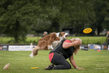 a woman is kneeling down while a dog tries to catch a frisbee in the air