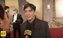 a man in a suit is being interviewed on a red carpet by et