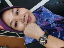 a woman wearing a purple scarf and a watch smiles for the camera