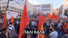 a crowd of people holding red and yellow flags with a sign in the background that says " pali kala "