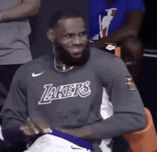 lebron james is wearing a lakers sweatshirt and smiling while sitting in the stands .