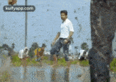 a man is standing in a puddle of water while a group of people are working in the background .