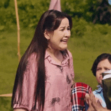 a woman in a pink shirt is standing in a field next to a boy holding a picnic blanket .