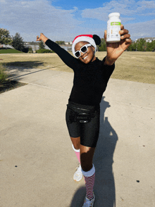 a woman wearing a santa hat holds up a bottle of herbalife vitamins