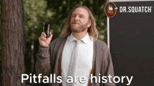 a man with long hair and a beard is holding a bottle in front of a blackboard that says pitfalls are history