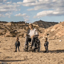 a man in a wheelchair is surrounded by two small men