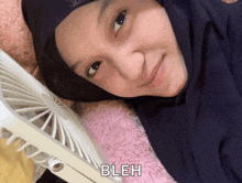 a woman in a black hijab is laying next to a fan and the word bleh is on the bottom