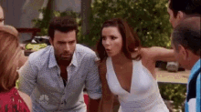 a man and a woman are standing next to each other in a crowd of people . the woman is wearing a white dress .