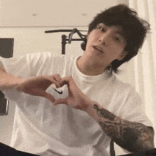 a man with a tattoo on his arm is making a heart with his hands