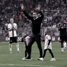 a man stands on a soccer field with his arms in the air while two little girls are standing behind him