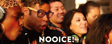 a man wearing glasses is sitting in a crowd of people and says nooice !