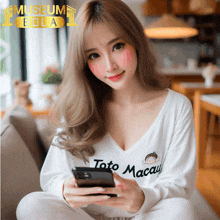 a woman wearing a white shirt that says toto macau holds a cell phone