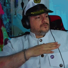 a man wearing a captain 's hat and headphones has a purple button on his pocket that says 15