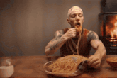 a man with tattoos is eating spaghetti with a knife and fork