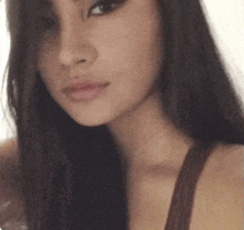 a close up of a woman 's face with long dark hair and a brown tank top .