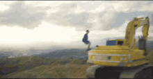 a man sitting on top of a yellow excavator on top of a hill .